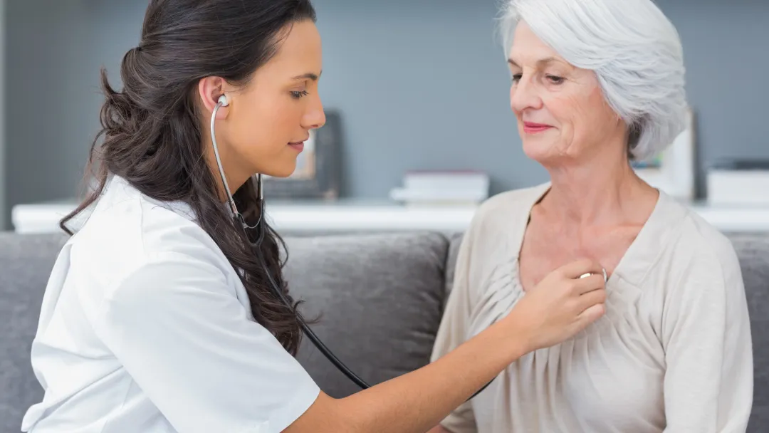 A nurse checks a patient's heart beat as they are both sitting down.