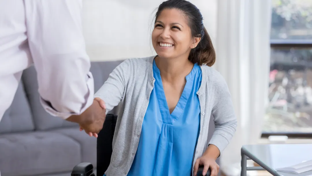 A woman in a wheelchair is shaking hands with a doctor.