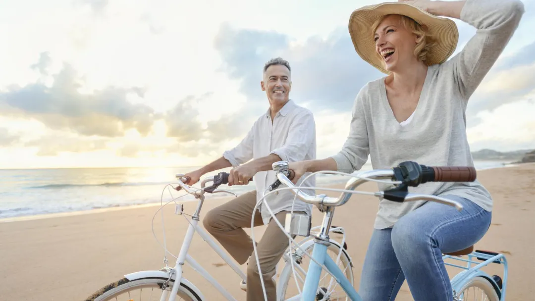 Man and woman in a hat riding bicycles on the beach at sunset. 