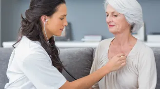 A nurse checks a patient's heart beat as they are both sitting down.