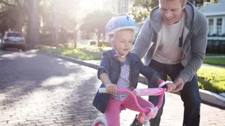 Father teaching his young daughter how to ride a pink bike in the street.