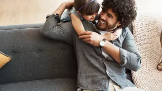A daugther hugging her father who is sitting in the couch.