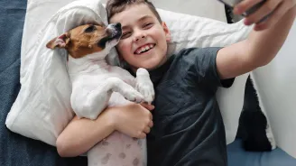 A Boy Takes a Selfie with His Dog While Laying on a Bed