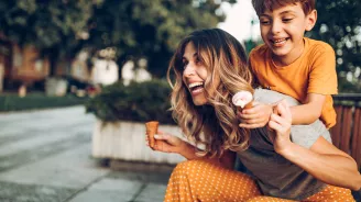 A Mother and Son Laugh and Play as They Eat Ice Cream Cones on a City Park Bench