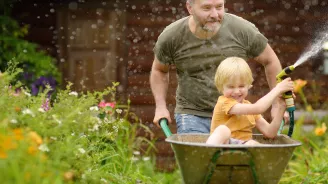 A Father and Son Spray a Garden Hose During a Wheelbarrow Ride