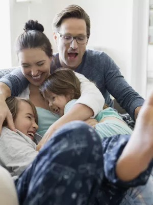 A Caucasian family laughs as they pile on the couch together.