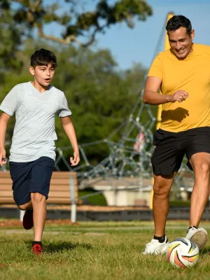 Son and father playing soccer in park