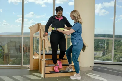 A healthcare worker helping a woman walk down stairs.