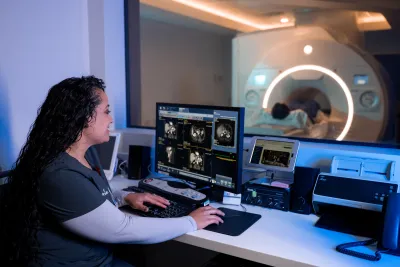 Imaging technician reviewing scans on a computer while a patient is receiving a MRI scan.
