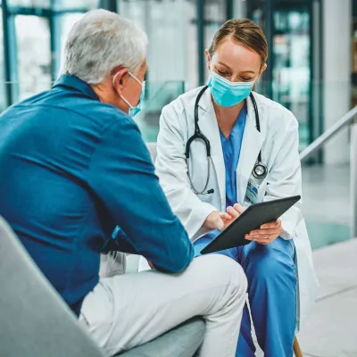 A female physician talking to a grey-haired gentleman with her tablet