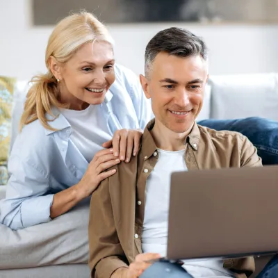 A white mature couple in their living room and on their laptop