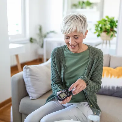 A mature woman taking an at-home diabetes test in her living room.