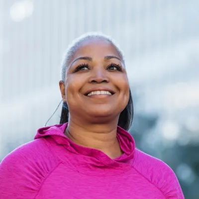 A smiling woman outside wearing a pink shirt for breast cancer awareness.