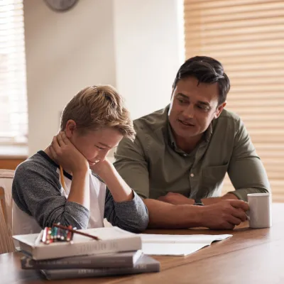 A Child Sits at the Kitchen Table Frustrated with School Work as His Father Tries to Help.