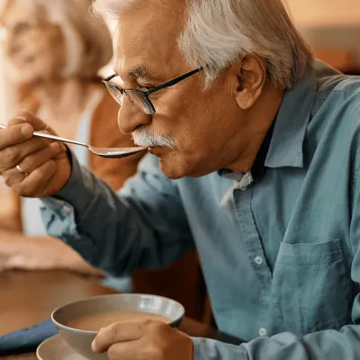 A Senior Man Eats Soup at the Dinning Room Table with Family