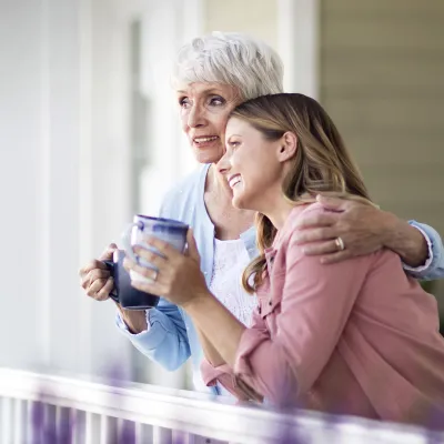 Two women converse on the front porch while drinking coffee.