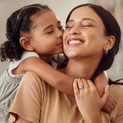 A Daughter Hugs Her Mom While Kissing Her on The Cheek 