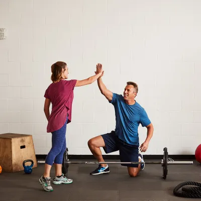 A Caucasian man and woman high-five while exercising at the gym.