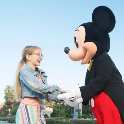Mickey Mouse holding a girls hands in front of Cinderella's Castle.