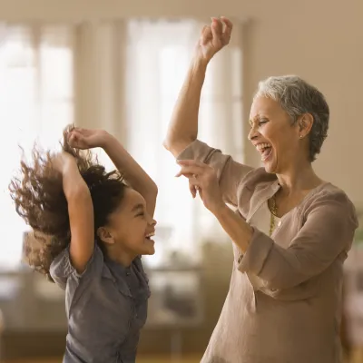 An elementary-aged girl and an older female relative dancing and smiling indoors