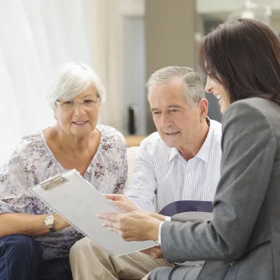 A female hospital staff member discusses information with an elderly couple.