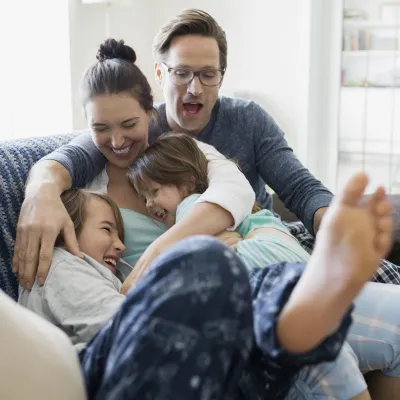 A Caucasian family laughs as they pile on the couch together.