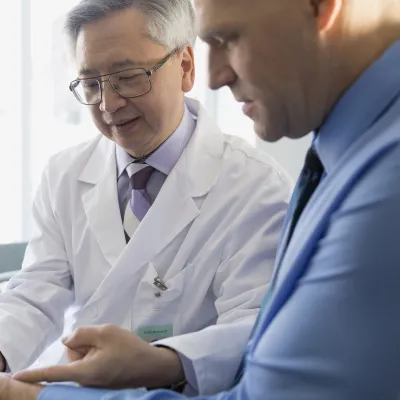 An Asian doctor identifies pain points on a male patient.