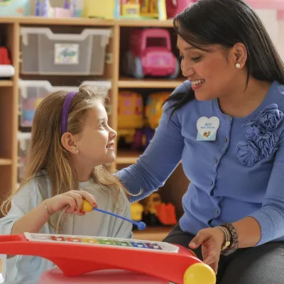 A young Caucasian girl plays the xylophone with her Asian music therapist.
