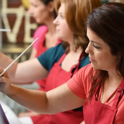A woman wearing a smock and painting in an art class