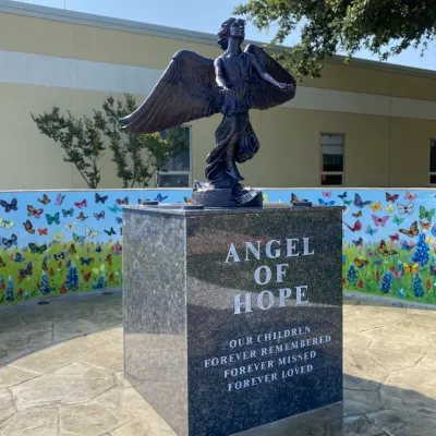Statue of an angel on a pedestal. The pedestal reads, "Angel of Hope. Our Children Forever Remembered, Forever Missed, Forever Loved."