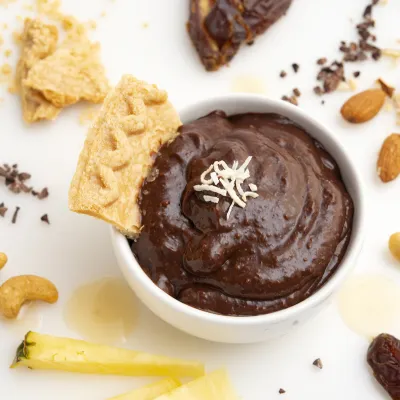 Carob pudding in bowl with a pie crust garnish, surrounded by decorative nuts