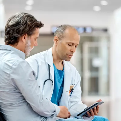 A physician and his male patient read documents together.