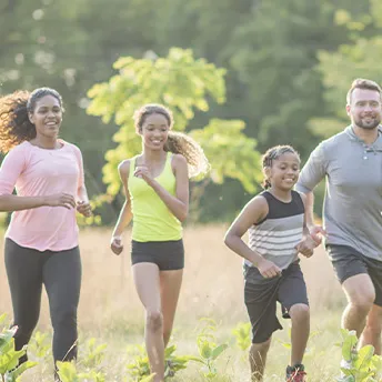 A family of four, running together outside in a field.