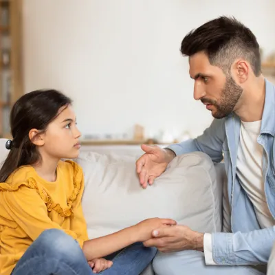 A father talks with his daughter while both are sitting on a couch.