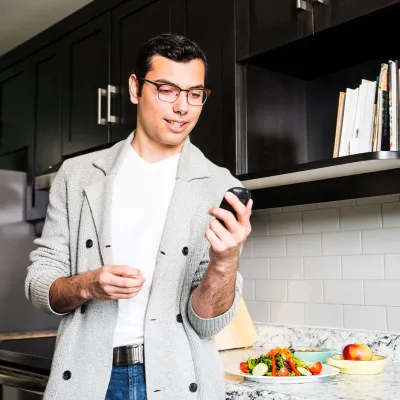 A Man Wearing Glasses Checks His Glucose Levels Before Eating a Healthy Meal in His Kitchen