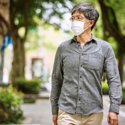 A man wearing a mask while walking outside. 