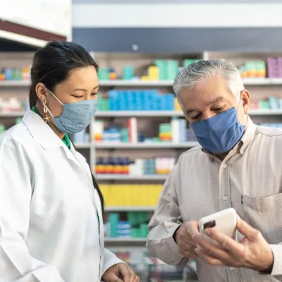 Older man talking with a pharmacist while both wear masks.