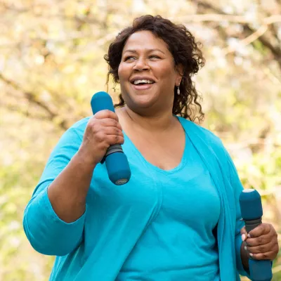 A woman exercising outdoors with hand weights. 