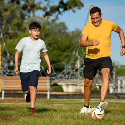 Son and father playing soccer in park