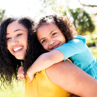 Mother carrying daughter on her back smiling
