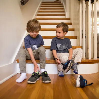Two brothers getting ready to go out while putting their shoes on.