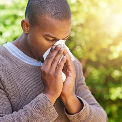 A black man blowing his nose while outside.