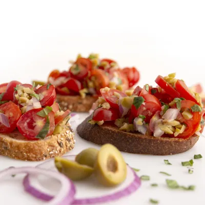 three pieces of bruschetta-topped toast with olive garnish