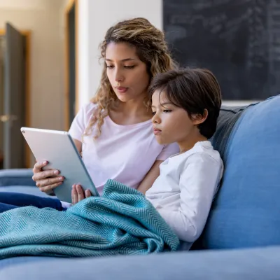 A mother and son sitting on a couch and using a tablet.