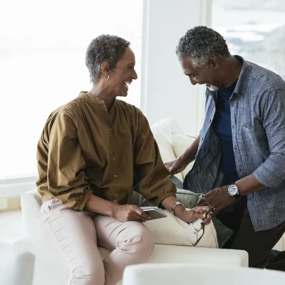 An African American couple smile and laugh on a couch in their home.
