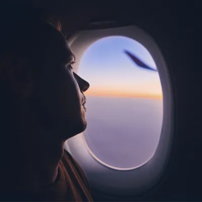 A man looks out the window of a plane during sunset.