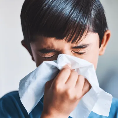 A young boy blowing his nose into a tissue.