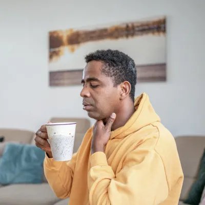 A man with a sore throat sips a cup of hot tea.