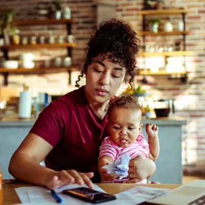 A mother holding her baby while using a calculator