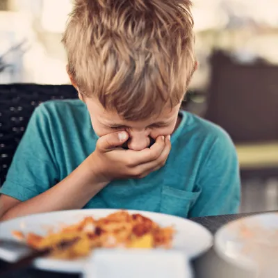 A young boy holding his hand over his mouth.